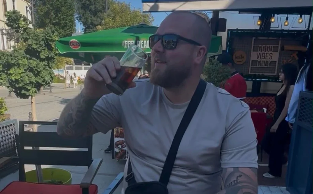 Luke Thurling outdoors holding a drink and smiling at camera.