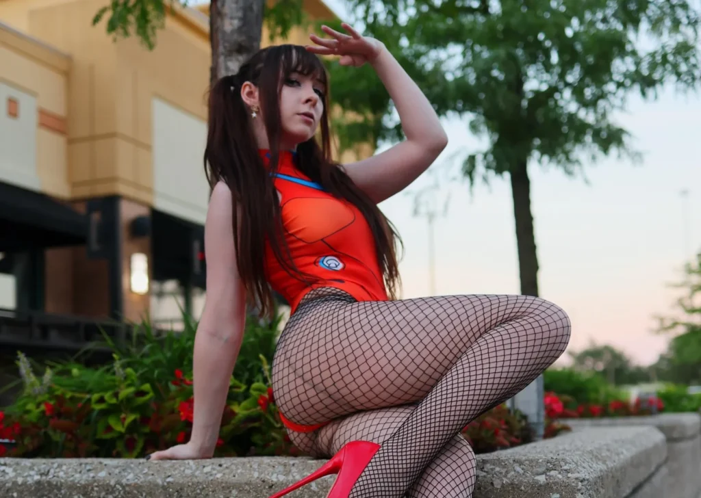 Woman in red outfit with fishnet stockings on heels crouching on concrete ledge outdoors.