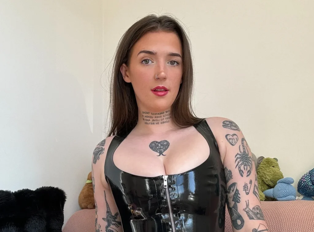 Woman with tattooed arms in black corset top on bed.
