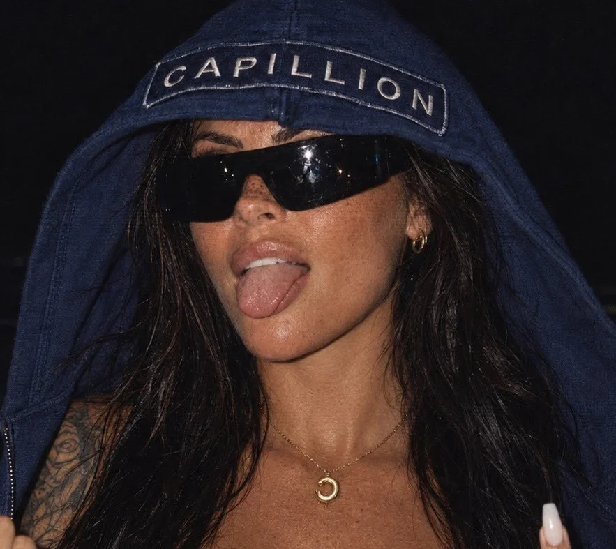 Woman wearing navy Capillion cap and sunglasses sticking tongue out.