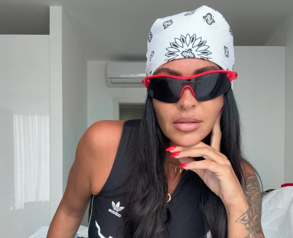 Woman in white cap and red sunglasses on bed in sports outfit.