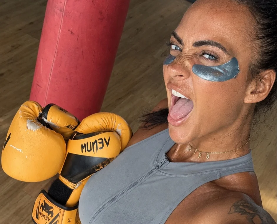 Woman in blue tank top wearing blue eye makeup at boxing gym.
