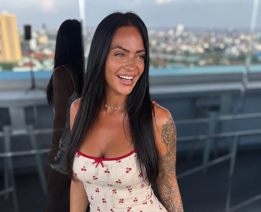 Woman on rooftop with city skyline in white floral dress.