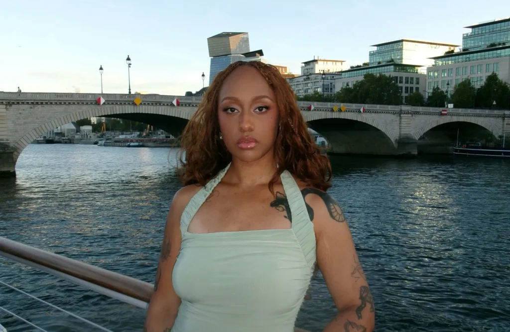 Woman in light green halter dress posing on boat railing by river.