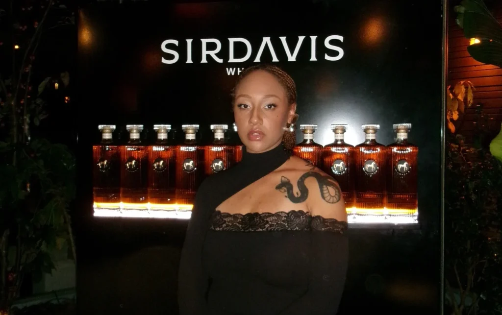 Woman in black top at SIRDAVIS event with lit display in background.