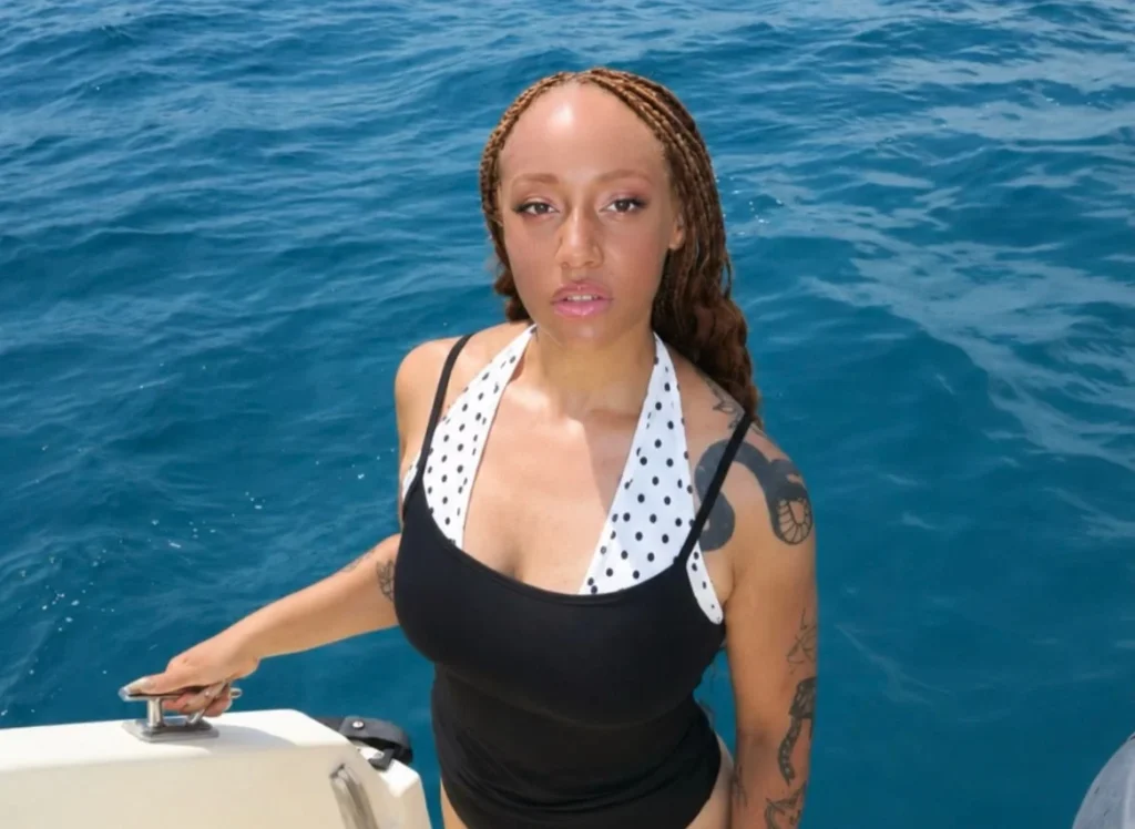 Woman in black and white swimsuit on boat, leaning on railing.