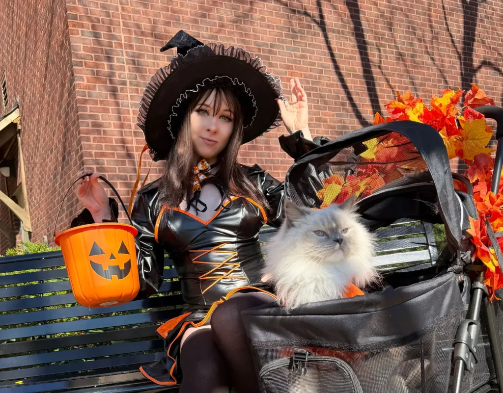 Woman in black costume on bench beside pram with cat and Halloween decorations
