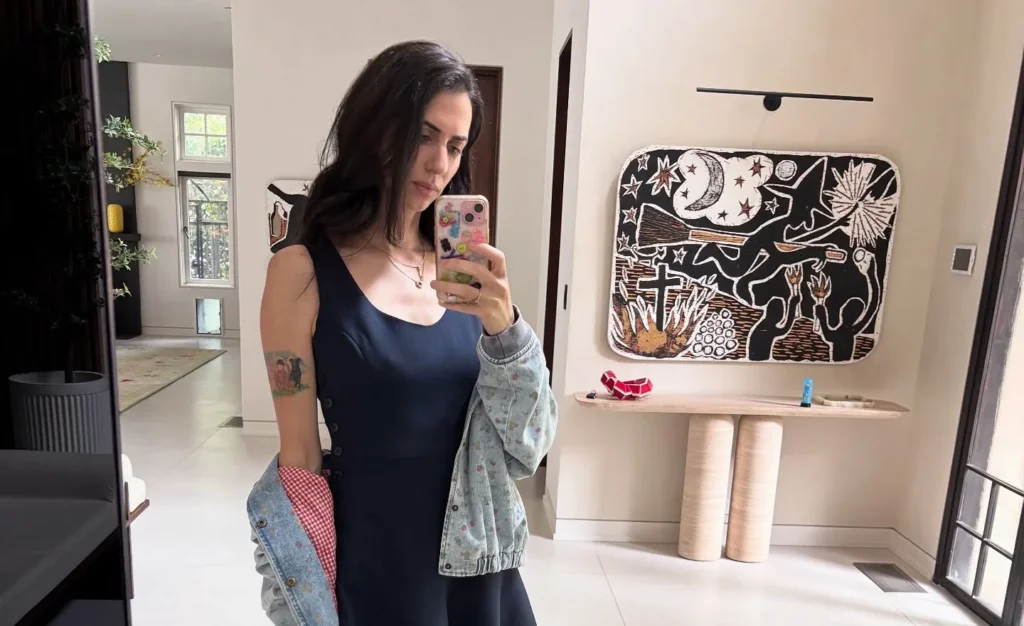 Hila Klein in navy dress and light cardigan, taking mirror selfie indoors