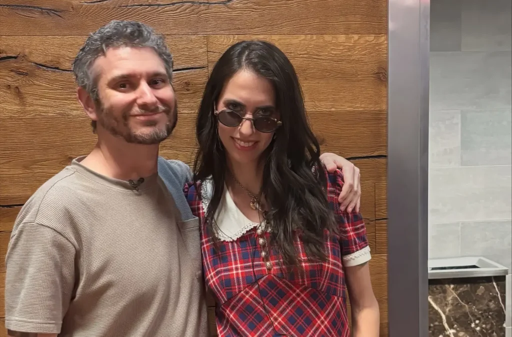 Ethan and Hila Klein standing together indoors, both smiling at camera