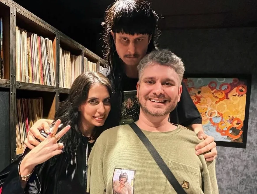 Three people posing together indoors with bookshelves visible in background