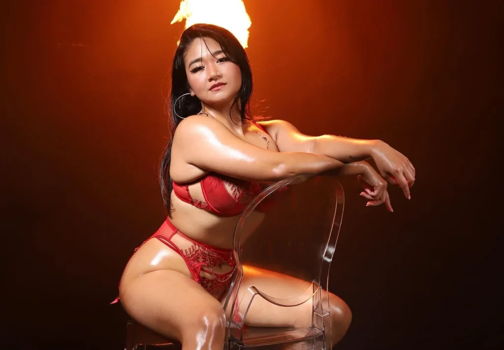 Woman in red lingerie posing on clear chair with fire backdrop.