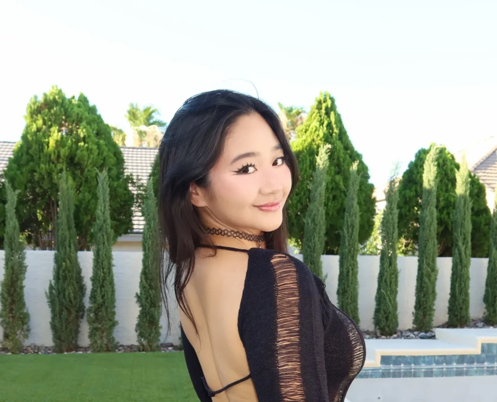 Woman in black open-back dress posing outdoors by white fence and pool.