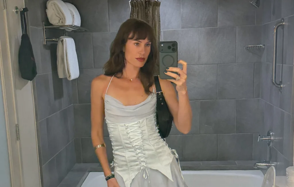 Woman in white dress taking mirror selfie in bathroom.