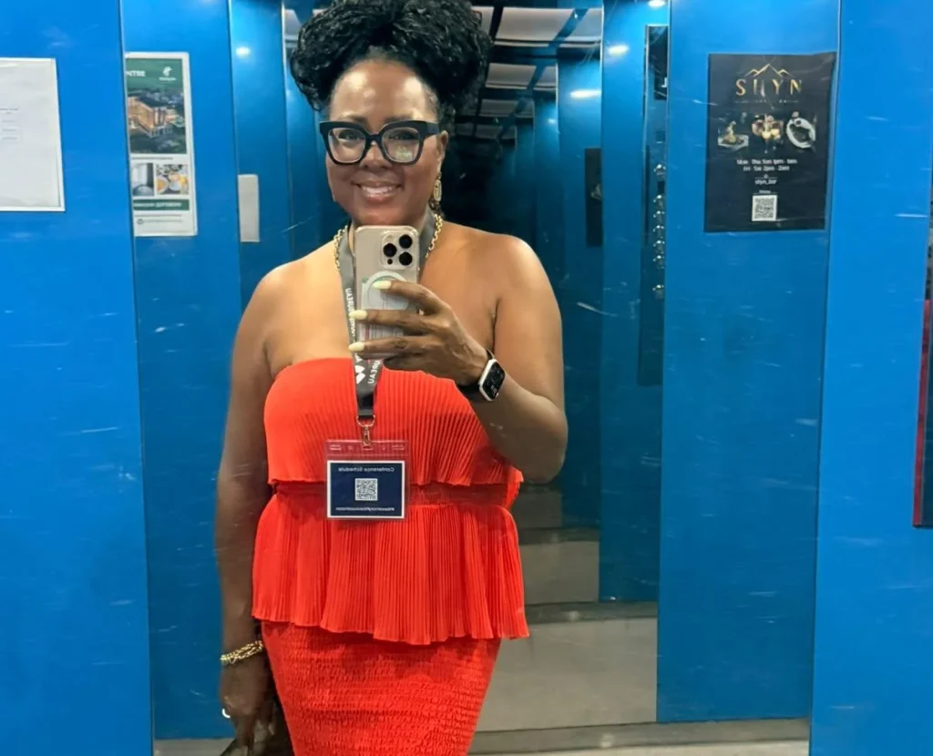 Tomiko Harvey in a red pleated dress taking a mirror selfie.
